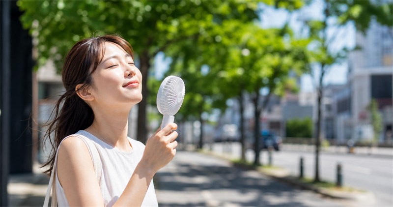 夏の街角でハンディファンを使う女性